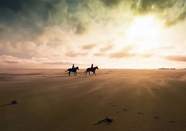 Photo of Couple riding horses across deserted sands at sunset