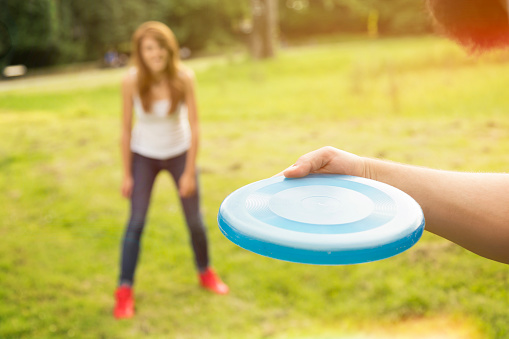 Young beautiful couple having fun and playing with frisbee on a meadow enjoying recreation in nature. Focus on the guy's hand