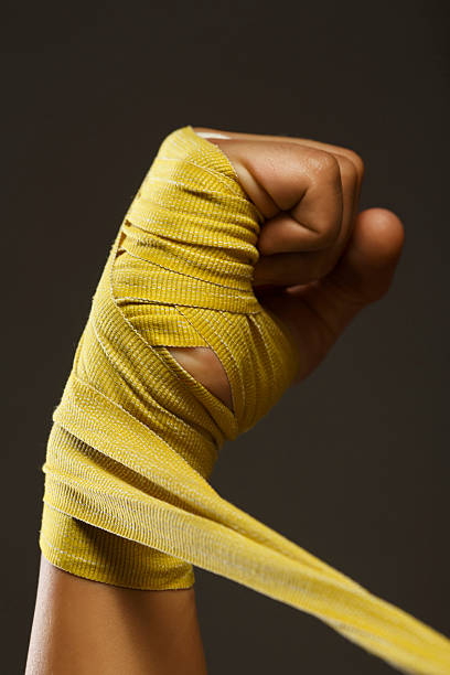 Fist Female kickboxing  Athletic woman wrapping hands with boxing wraps Fist. Female kickboxing fighter.  Athletic young woman preparing before sports training, wrapping hands with yellow boxing wraps.  Health club. kickboxing photos stock pictures, royalty-free photos & images