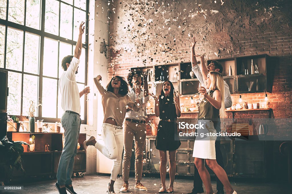 Just having fun. Full length of cheerful young people throwing confetti and jumping while enjoying home party on the kitchen Party - Social Event Stock Photo