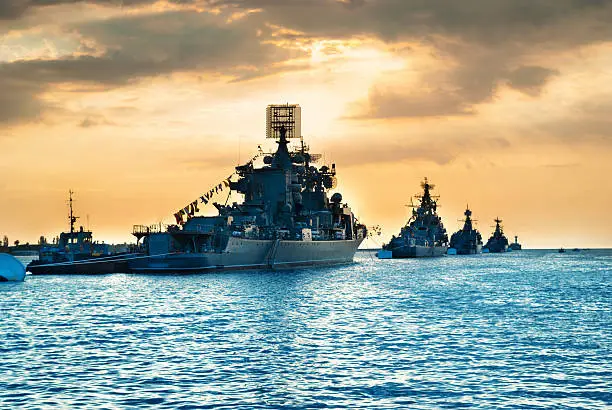 Military navy ships in a sea bay at sunset time