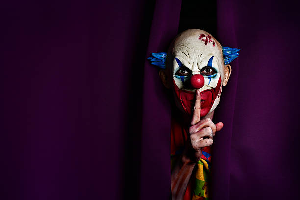scary evil clown asking for silence a scary evil clown peering out from a purple stage curtain, with his forefinger in front of his lips, asking for silence, with a negative space on one side face paint halloween adult men stock pictures, royalty-free photos & images