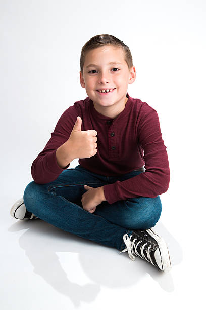 Smiling boy sitting with thumbs up stock photo