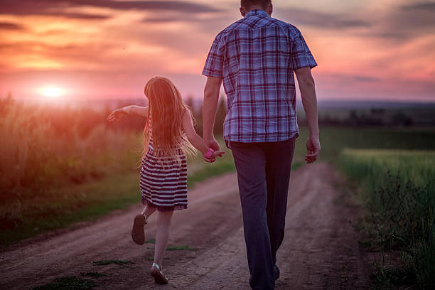 istock Dad and daughter walking in field at sunset 612029690