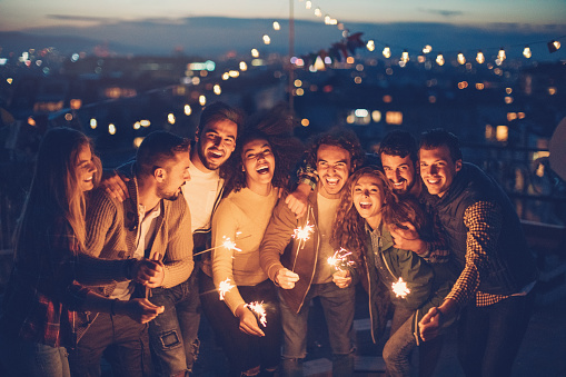 Group of young people holding flaring sparklers celebrating in the evening on a rooftop.