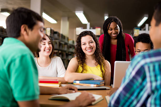 istock Latin female student sitting with friends at the library 612239100