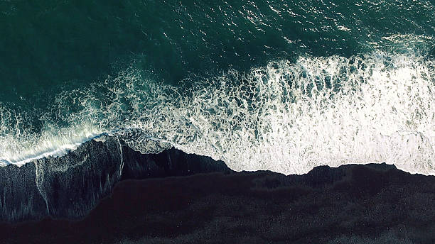 Aerial tracking shot Cold ocean waves washing down the black sand beach making a lot of ocean foam. The video is taken by drone which goes down to 350 meters and rotates. atlantic ocean photos stock pictures, royalty-free photos & images