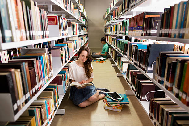 istock Student reading a book on the floor of a library 612243500