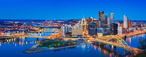 Panoramic cityscape photo of downtown Pittsburgh, Pennsylvania, USA, illuminated at twilight blue hour. It is located at the confluence of the Allegheny and Monongahela rivers.