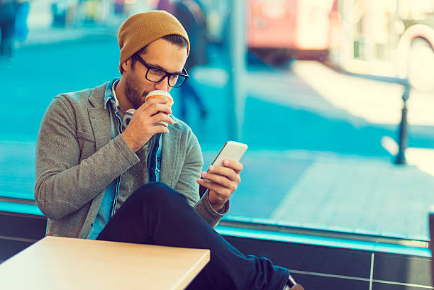 잘 생긴 남자 커피를 마시고 그의 smarptphone를 사용 하 여 - male beauty audio 뉴스 사진 이미지