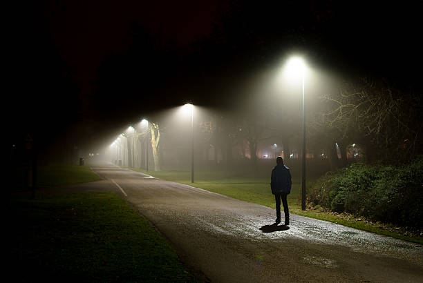 una sola persona caminando por la calle en la noche oscura - una sola vía fotografías e imágenes de stock