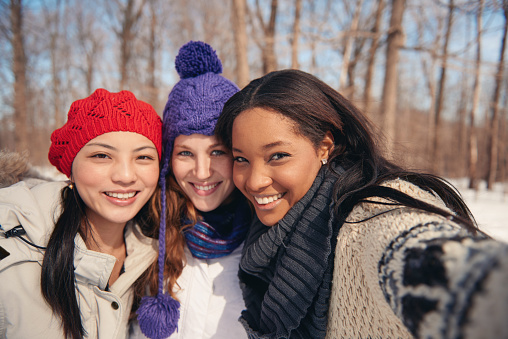 Group of millenial young female adult friends enjoying wintertime and in a snow filled park