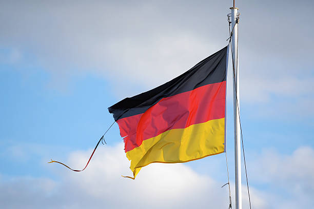istock Frayed flag of Germany  against a blue sky with clouds 612250712