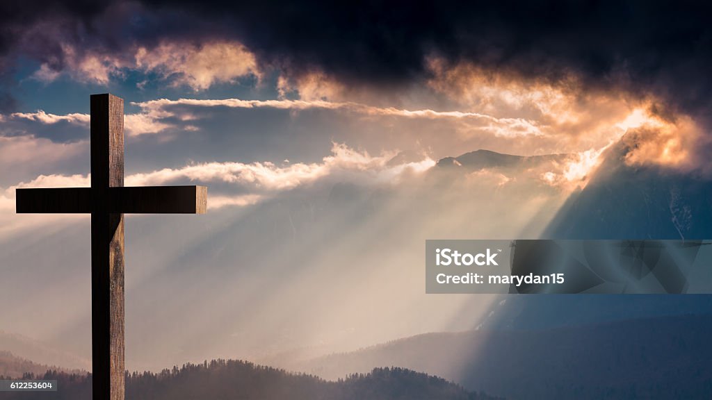 Jesus Christ wooden cross on a dramatic, colorful sunset     Jesus Christ cross. Christian wooden cross on a background with dramatic lighting, colorful sunset, twilight and orange -  purple clouds and sky.  Easter, resurrection,Good Friday concept Religious Cross Stock Photo