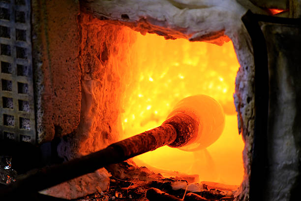 Manufacturing glass in a traditional oven, the glassblower working on a handmade vase of melted glass on a rod, selected focus and narrow depth of field