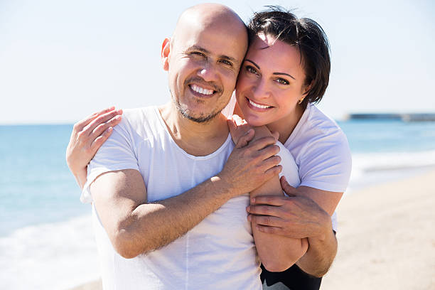 Couple embracing on the beach Close-up portrait of a happy mature man and a woman happily embracing each other on the beach two men same clothes stock pictures, royalty-free photos & images