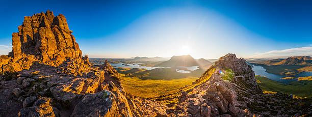 Warm early morning sunlight bursting over the mountain peaks of Cul Mor, Suilven and Canisp to the dramatic wilderness landscape of Inverpolly and Assynt illuminating the golden rocks and heather of Stac Pollaidh, deep in the Sutherland Highlands of Scotland.