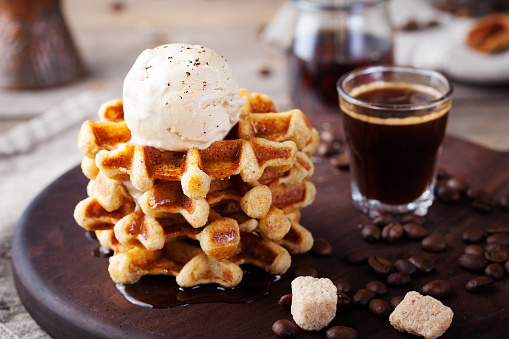 Fresh whole wheat waffles with ice cream, maple syrup and coffee on a wooden background