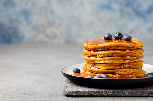 Pumpkin pancakes with maple syrup and blueberries on a plate. Grey stone background Copy space