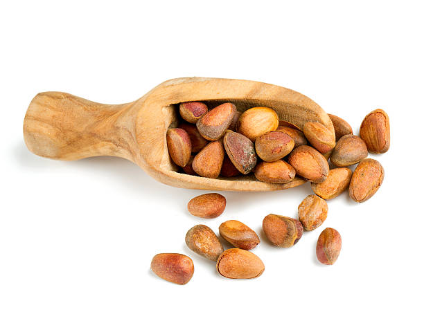 кедровые орехи в деревянной мерной ложке изолированы на белом фоне - pine nut nut isolated pine cone стоковые фото и изображения
