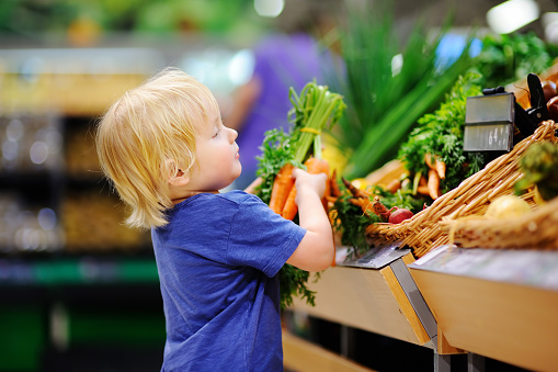 Cute toddler boy in a food store or a supermarket choosing fresh organic carrots. Healthy lifestyle for young family with kids