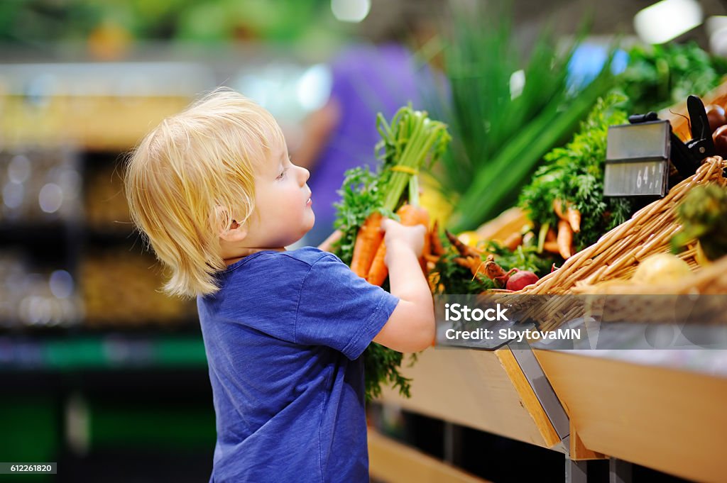 Menino fofo em supermercado escolhendo cenouras orgânicas frescas - Foto de stock de Criança royalty-free