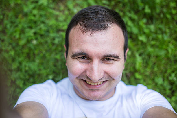istock Man smiling and lying down on the grass,making selfie 612263408
