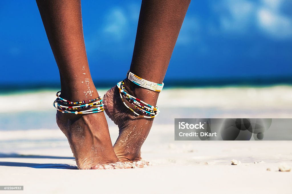 Tropical vacation Beautiful female legs on a white sandy beach. dressed in traditional Maasai jewelry. Zanzibar. Tanzania Women Stock Photo