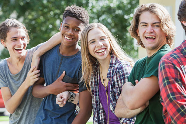 Multiracial group of teenagers handing out outdoors A multi-ethnic group of teenagers hanging out together outdoors. They are in a row, laughing and smiling. happy young teens stock pictures, royalty-free photos & images