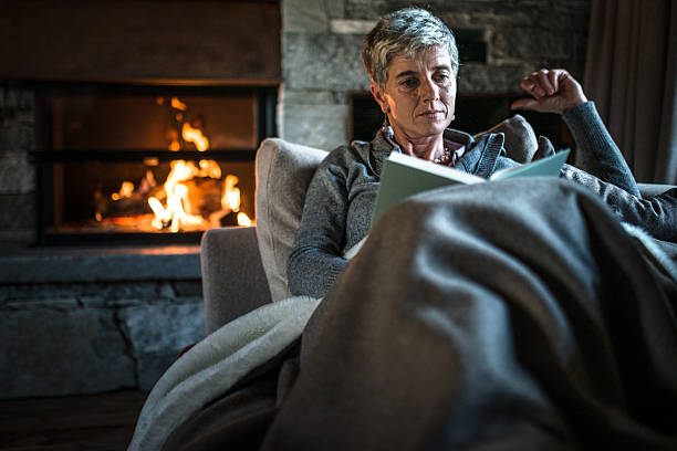 frau liest ein buch auf dem sofa - blanket fireplace winter women stock-fotos und bilder