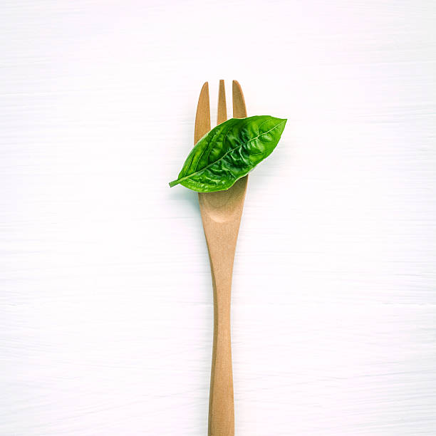istock Closeup  fresh sweet basil leaves with fork  on white. 612370660
