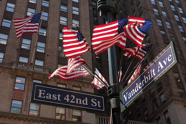 Multiple American flags blowing freely in the wind on top of a street sign in New York city, New York