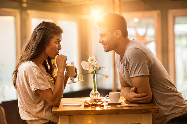 Young couple in love spending time together in a cafe. Young woman drinking coffee and communicating with her smiling boyfriend in a cafe. flirty stock pictures, royalty-free photos & images