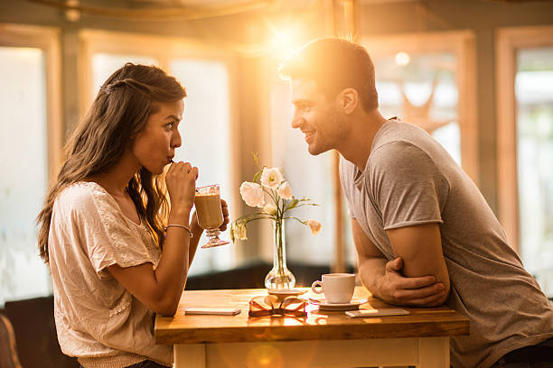 Young couple in love spending time together in a cafe. Young woman drinking coffee and communicating with her smiling boyfriend in a cafe. Romance stock pictures, royalty-free photos & images