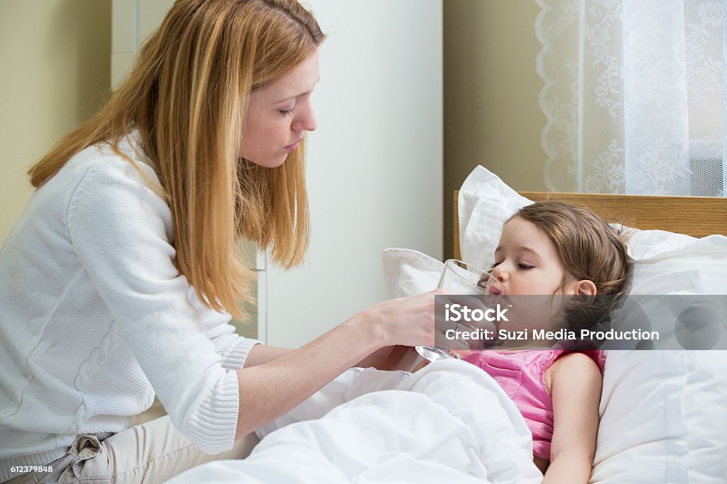 Sick child with high fever Worried mother giving glass of water to her ill kid. Sick child with high fever laying in bed. Hand on forehead. Child Stock Photo