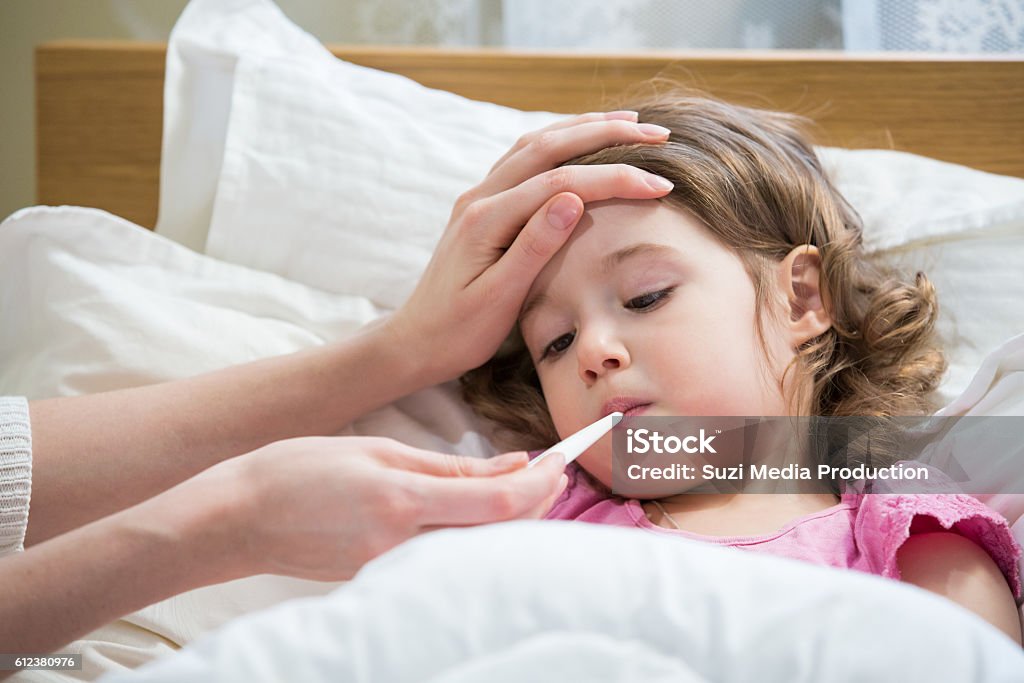 Sick child with high fever Mother measuring temperature of her ill kid. Sick child with high fever laying in bed and mother holding thermometer. Hand on forehead. Child Stock Photo