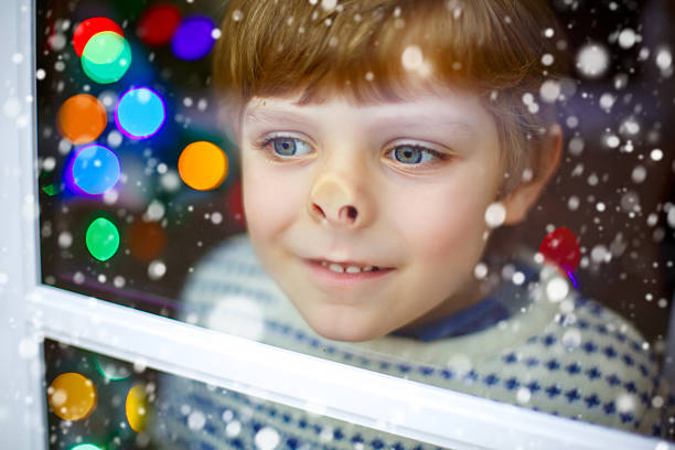 ragazzo vicino alla finestra e guardando all'aperto a natale - christmas window santa claus lighting equipment foto e immagini stock