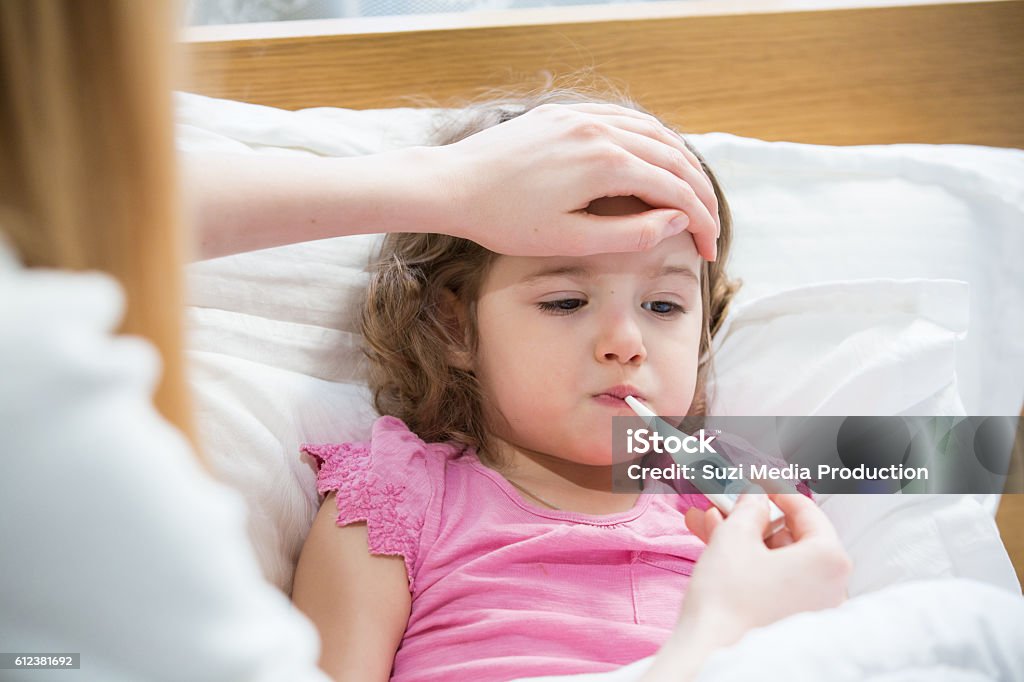 Sick child with high fever Mother measuring temperature of her ill kid. Sick child with high fever laying in bed and mother holding thermometer. Hand on forehead. Child Stock Photo