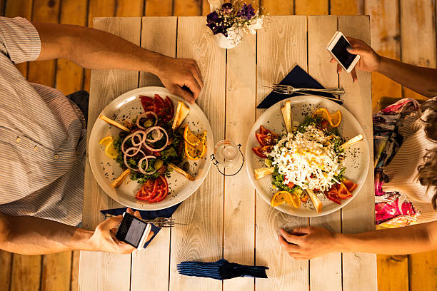 High angle view of unrecognizable couple text messaging on mobile phones during a lunch in the restaurant and ignoring each other.