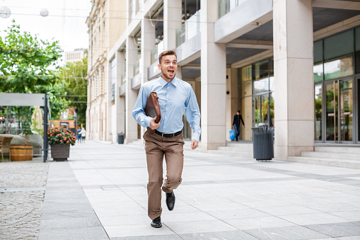 Young businessman with a briefcase running in a city street. Hurrying to work.