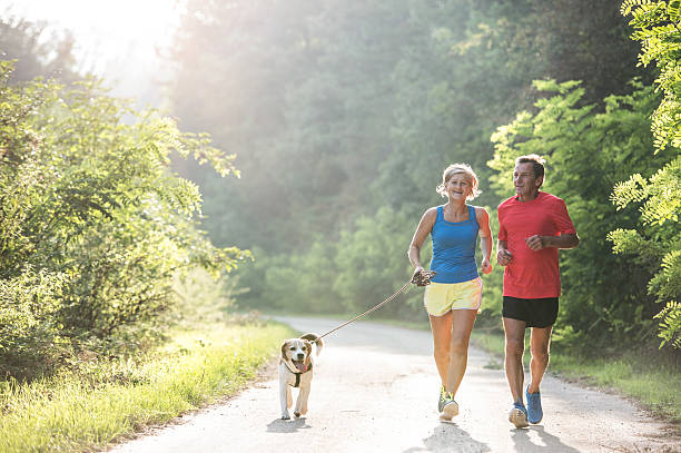 pareja de ancianos con perro corriendo en la naturaleza verde y soleada - action senior adult lifestyles couple fotografías e imágenes de stock
