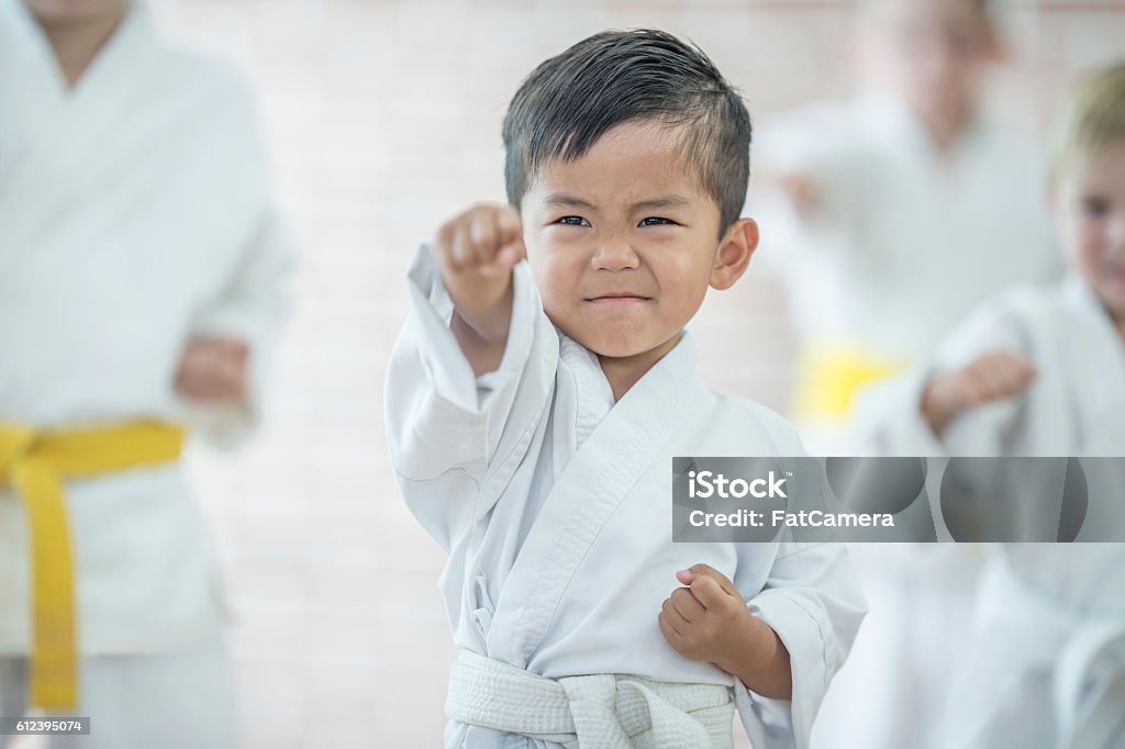 Cute Little Boy Taking Karate A multi-ethnic group of elementary age children are taking a karate class together at a health club. A cute little boy is raising his fist in the air to punch. Child Stock Photo