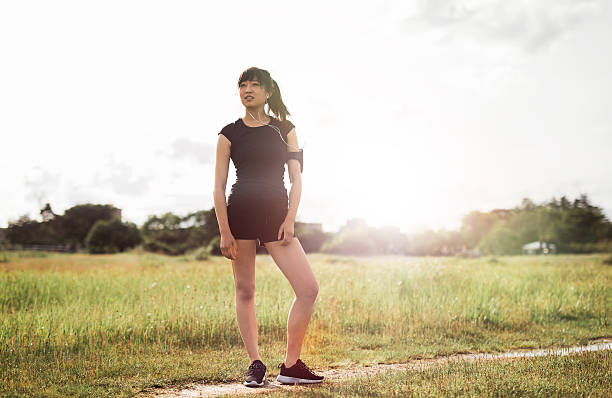 Full length portrait of female runner standing outdoors in morning. Chinese female model in sports wear ready for running workout.
