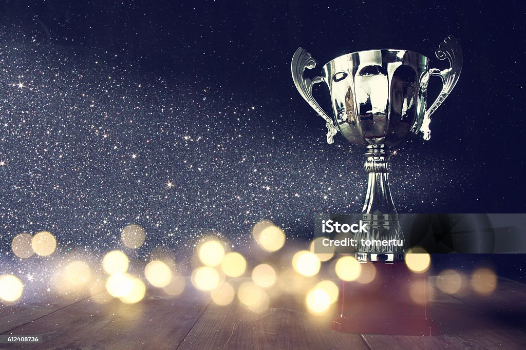 low key image of trophy over wooden table low key image of trophy over wooden table and dark background, with abstract shiny lights Award Stock Photo