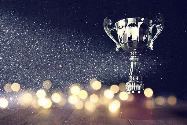 low key image of trophy over wooden table low key image of trophy over wooden table and dark background, with abstract shiny lights trophy award stock pictures, royalty-free photos & images