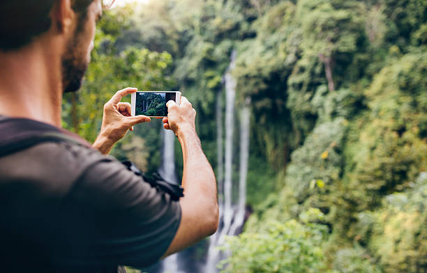 istock Man taking photos of waterfall with his cellphone 612410122