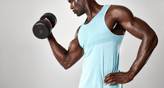 Mixed race man exercising with hand weights against grey background. Young fit man lifting a dumbbell.