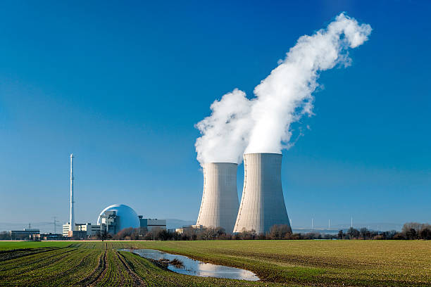 Nuclear power station Grohnde with steaming cooling towers Nuclear power station countryside with two steaming cooling towers and blue sky.  nuclear reactor stock pictures, royalty-free photos & images