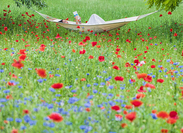 Young woman lying on hammock in garden reading book.