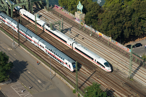 Cologne, Germany - September 22, 2016: view to the railroad with two trains in German, Cologne. An ICE and an IC train. They driving over the Hohenzollern bridge in Cologne. People walking at the street. 